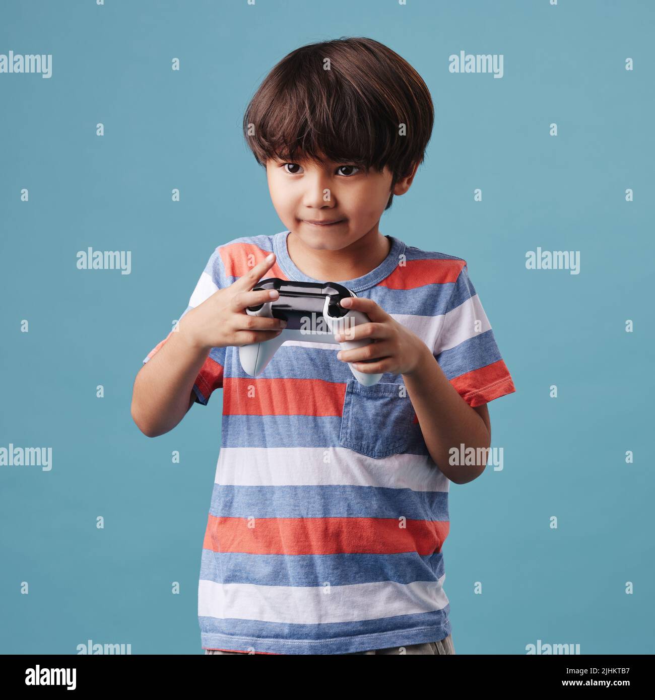 Giovane ragazzo misto da corsa in piedi e tenendo un controller console mentre si gioca un videogioco su sfondo blu. Divertimento e giochi sono una buona attività Foto Stock