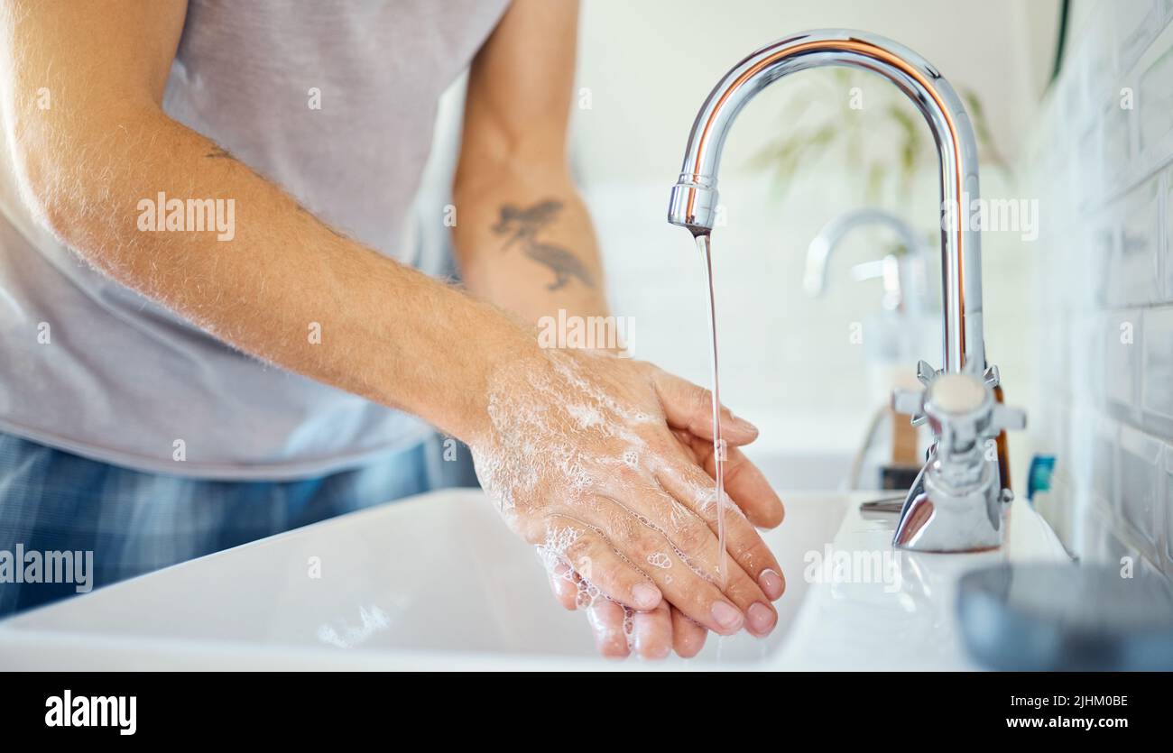 Un uomo sconosciuto che lava le mani in un bagno a casa. Maschio non riconoscibile usando sapone per uccidere i batteri e prevenire la diffusione di virus in un bacino Foto Stock