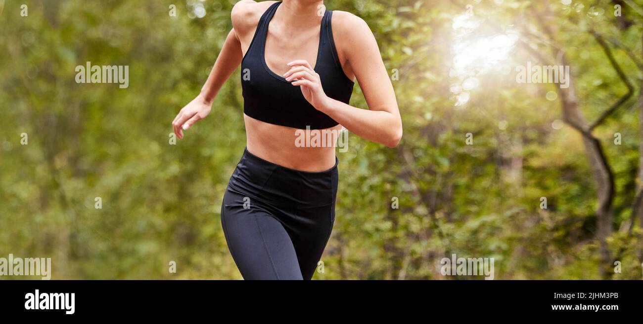 Primo piano di un corpo femminile vestito da allenamento mentre fuori per una corsa in un parco o nella natura in una giornata di sole. Donna che si esercita e vive un sano Foto Stock