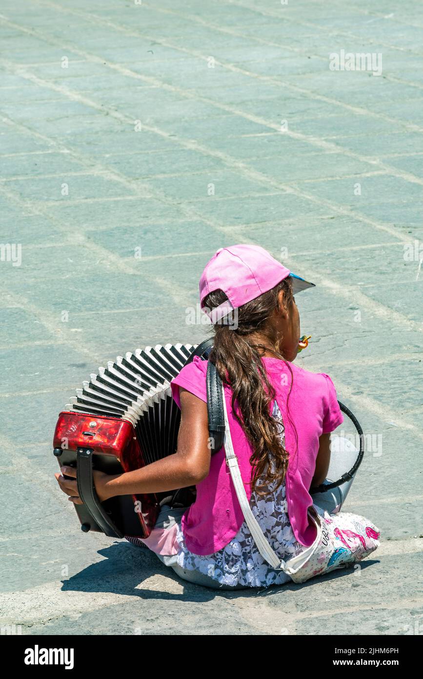 giovane ragazza che gioca a un fisarmonicista per le strade di heraklion, sull'isola greca di creta, implorando soldi. artista di strada in grecia. Foto Stock