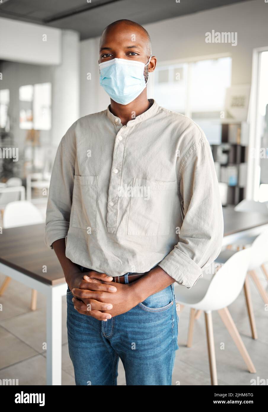 Giovane uomo d'affari afroamericano in piedi in un ufficio che indossa una maschera al lavoro. Maschio business professionale indossare una maschera di protezione da un virus e. Foto Stock
