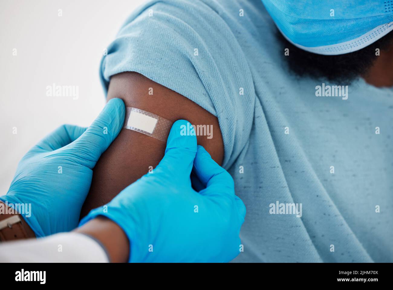 Primo piano di un medico che applica un cerotto sul braccio di un paziente. Mano di un medico gp come loro applicano un gesso tagliato. Medico afroamericano che applica un Foto Stock