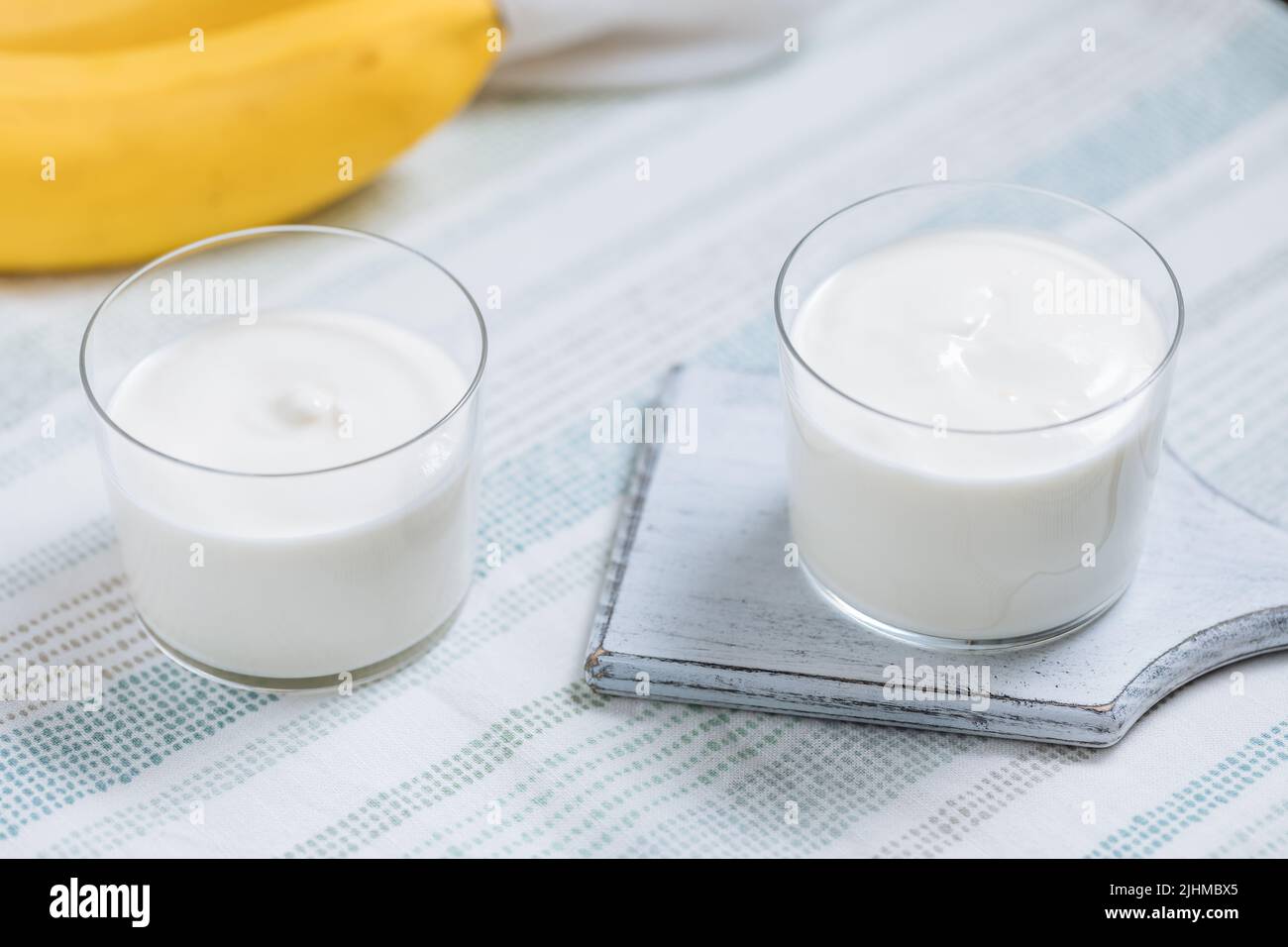 Banana e yogurt in vetro su bordo azzurro con banana sullo sfondo. Colazione sana. Dolce. Stile di vita fitness. Dessert vegetariano sano. Foto Stock