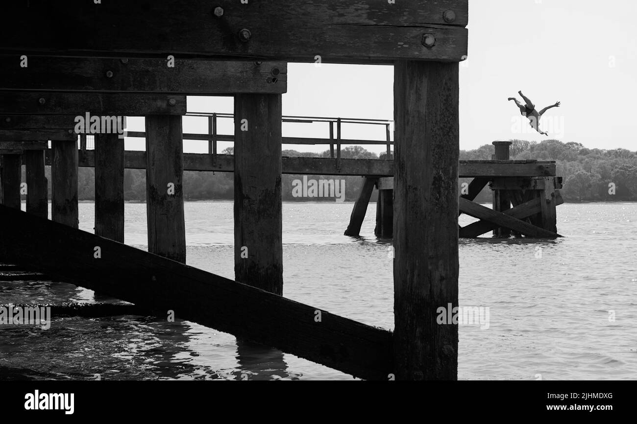 Boy Jumping dal Wooden Pier sulla spiaggia di Lake Pier sulla costa settentrionale di Poole Harbour, Regno Unito Foto Stock