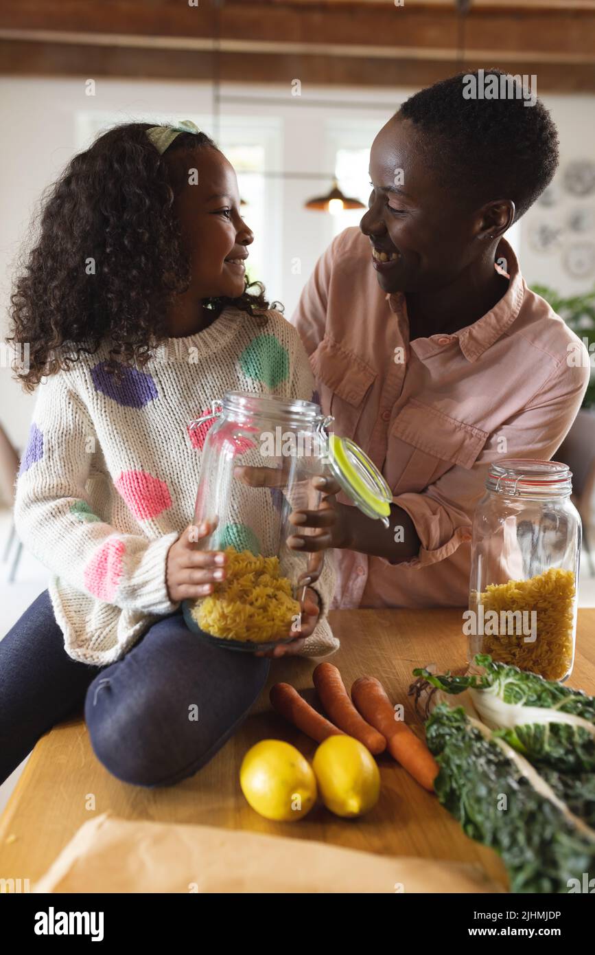Immagine verticale di felice madre e figlia afroamericana che tiene il vaso con la pasta Foto Stock
