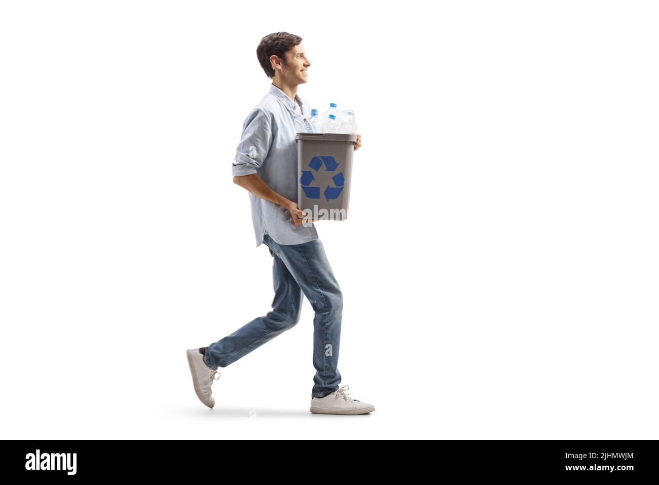 Giovane uomo che cammina e trasporta un cestino di riciclaggio con bottiglie di plastica isolate su sfondo bianco Foto Stock