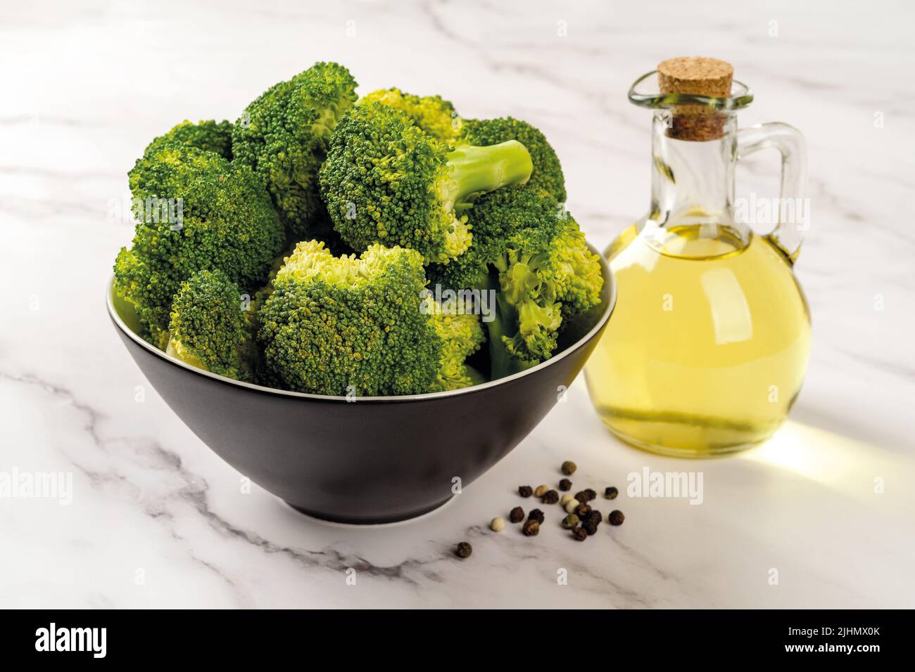 Broccoli freschi e olio d'oliva sul piano di appoggio in marmo. Broccoli verdi crudi in un recipiente nero e caraffa di vetro con olio di girasole. Cibo a bassa calorie. Foto Stock