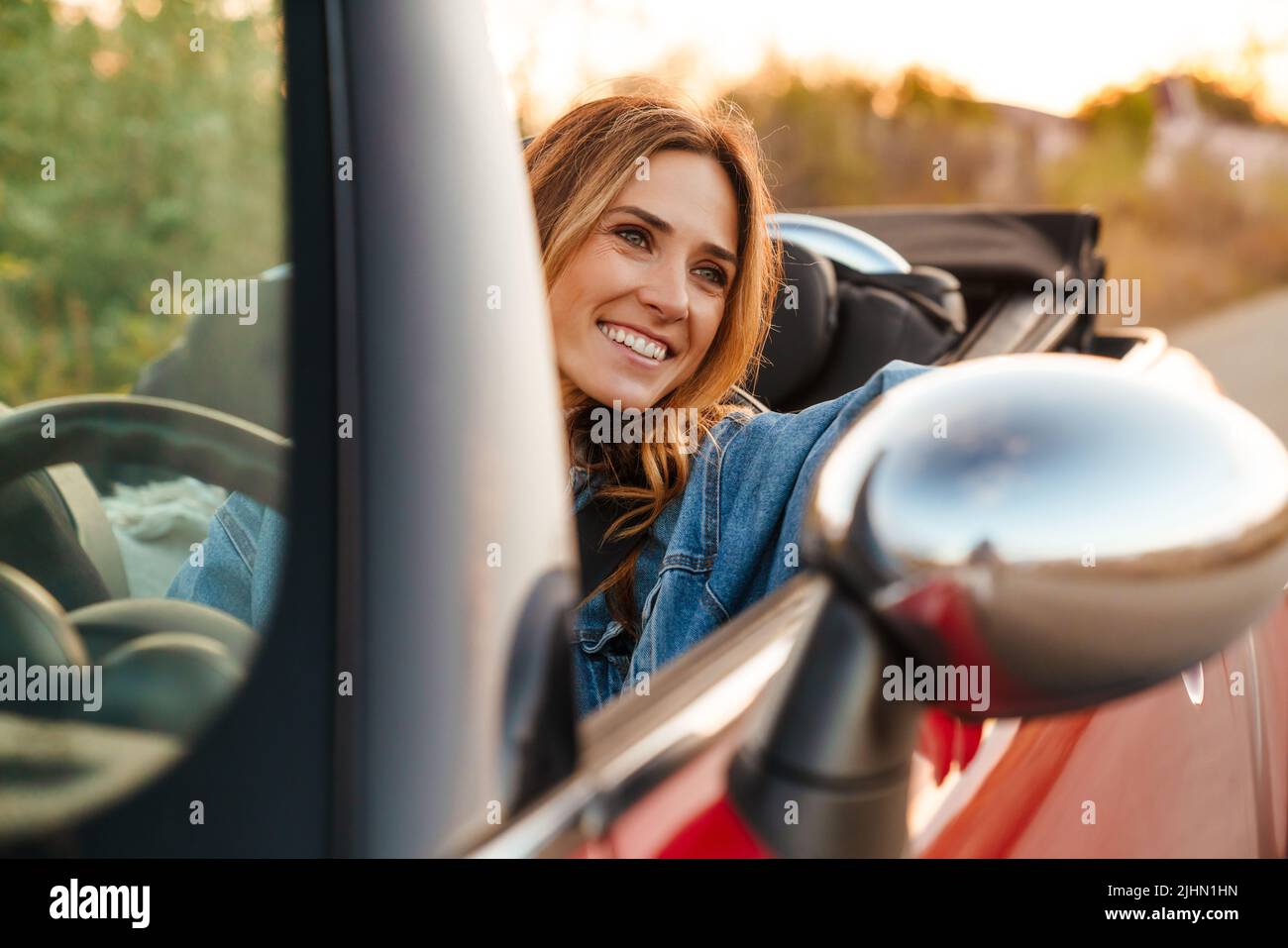Donna zenzero bianca sorridente mentre guida l'auto durante il viaggio Foto Stock