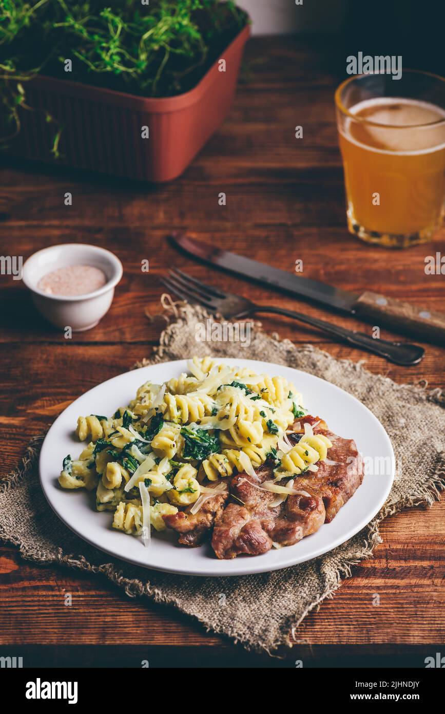 Bistecca al collo di maiale e pasta cremosa con spinaci e timo Guarnito con parmigiano grattugiato su piatto bianco Foto Stock