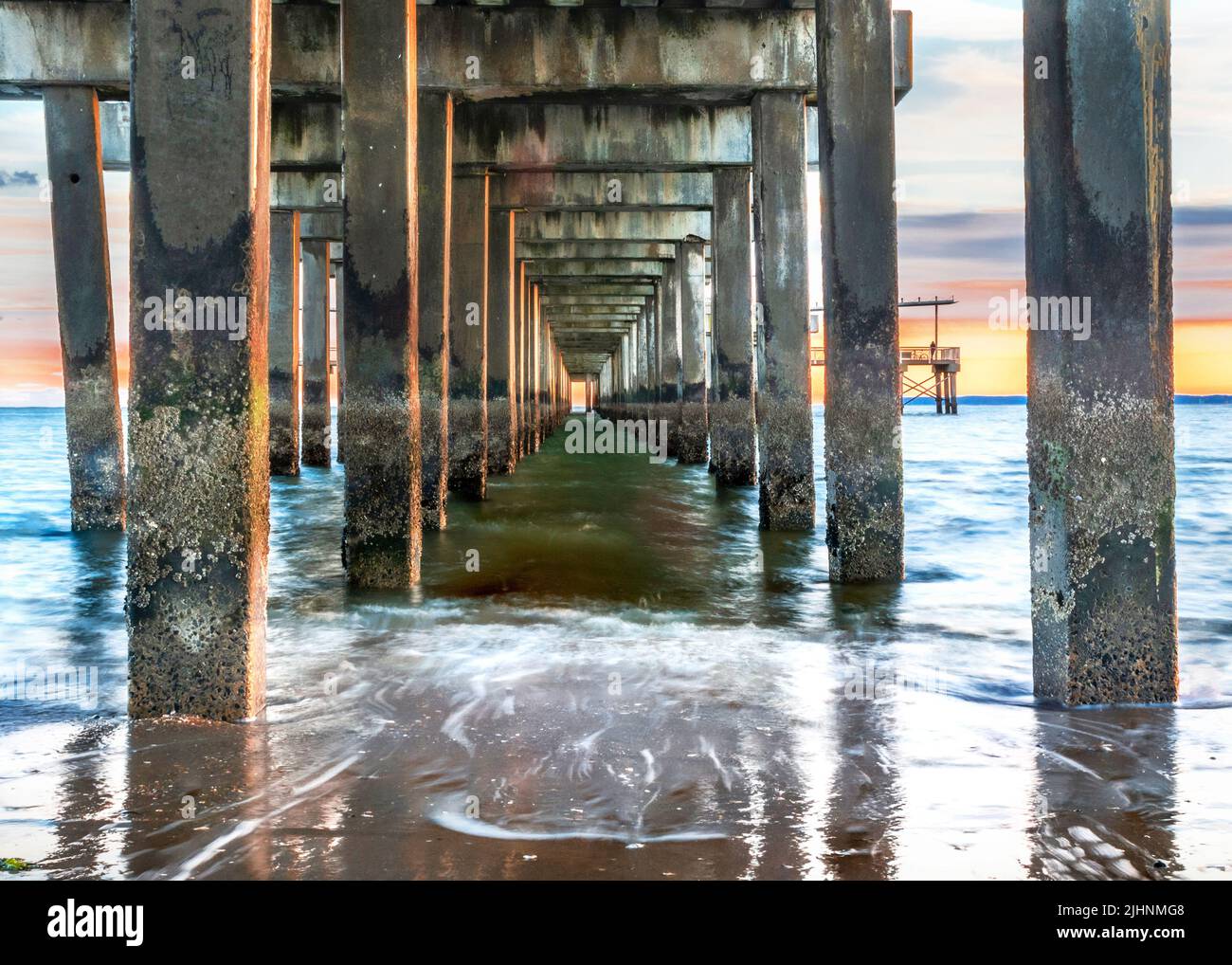 Alba e onde sotto il molo alla spiaggia Foto Stock