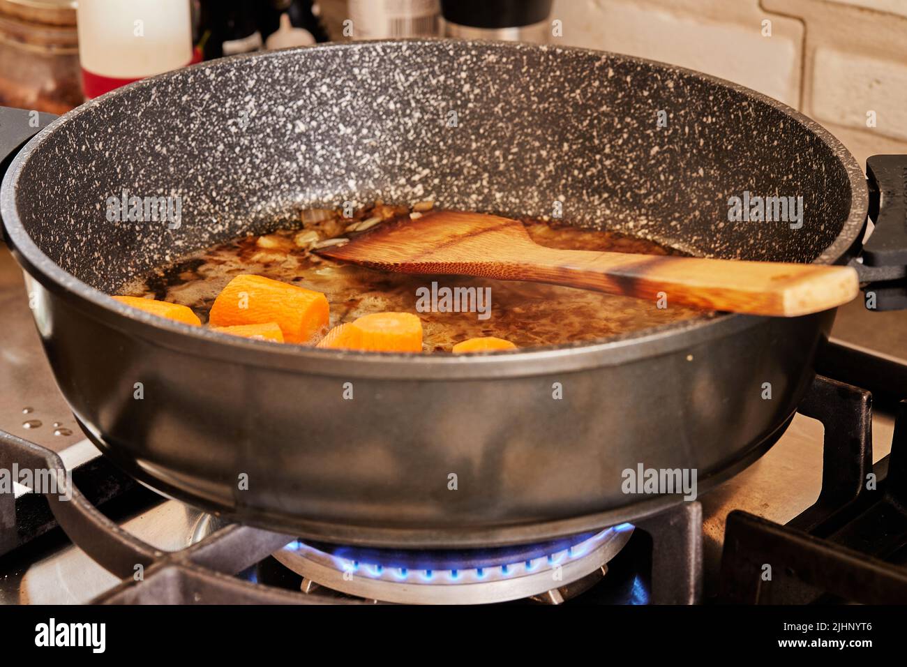 Le carote vengono fritte in padella su una stufa a gas per fare il pesce stufato con funghi e patate Foto Stock
