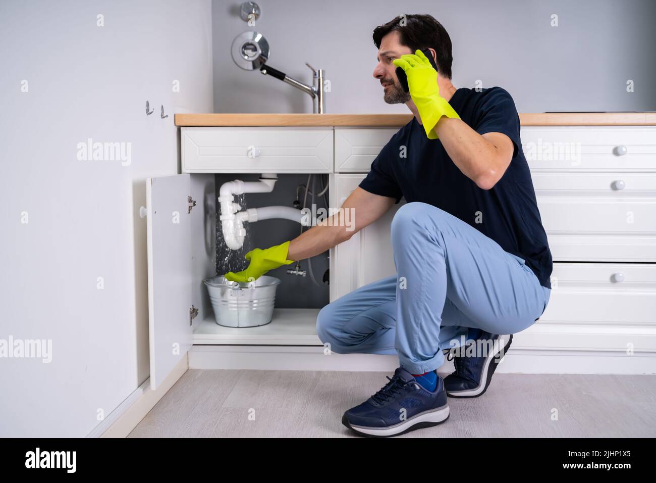 Triste giovane uomo che chiama idraulico di fronte a perdita d'acqua da Sink Pipe Foto Stock