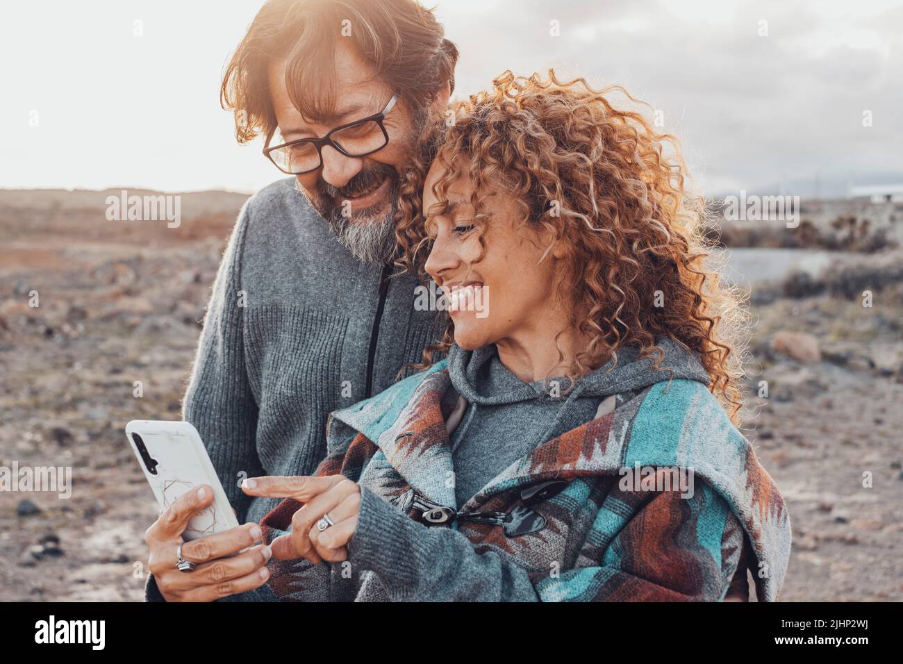 Uomo e donna che usano l'app per cellulare all'aperto sorridendo e godendo della connessione tecnologica. La coppia felice comunica con il cellulare mobile insieme. Touri Foto Stock