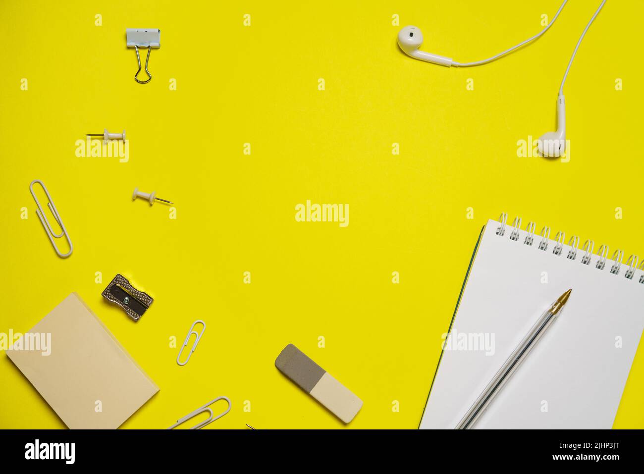 Cuffie bianche cablate con blocco note a molla, clip di carta e pulsanti, cancelleria da scuola su sfondo giallo con spazio per la copia Foto Stock