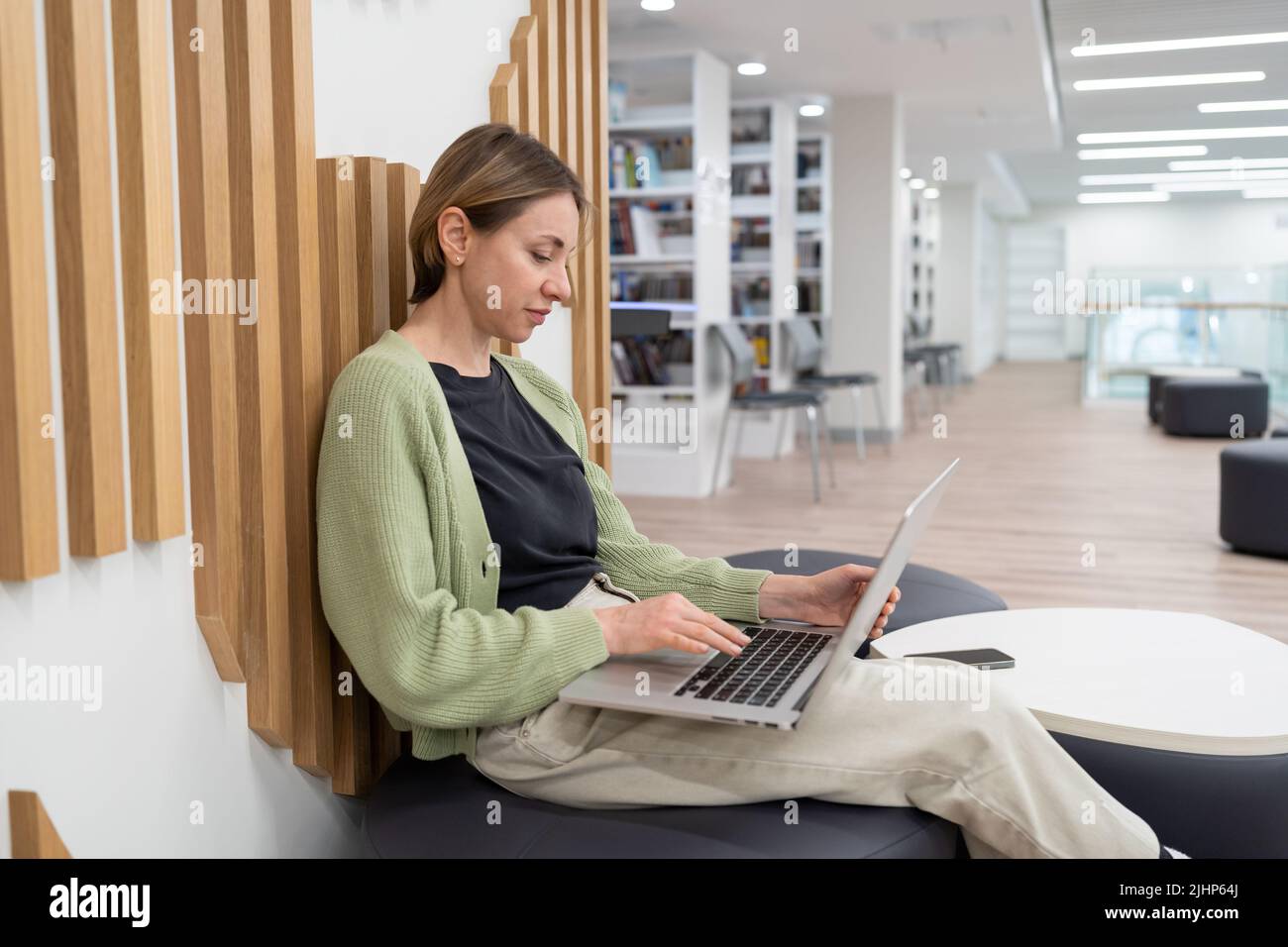 Autore freelance focalizzato donna che lavora su un notebook in biblioteca. Freelance dopo il 40 Foto Stock