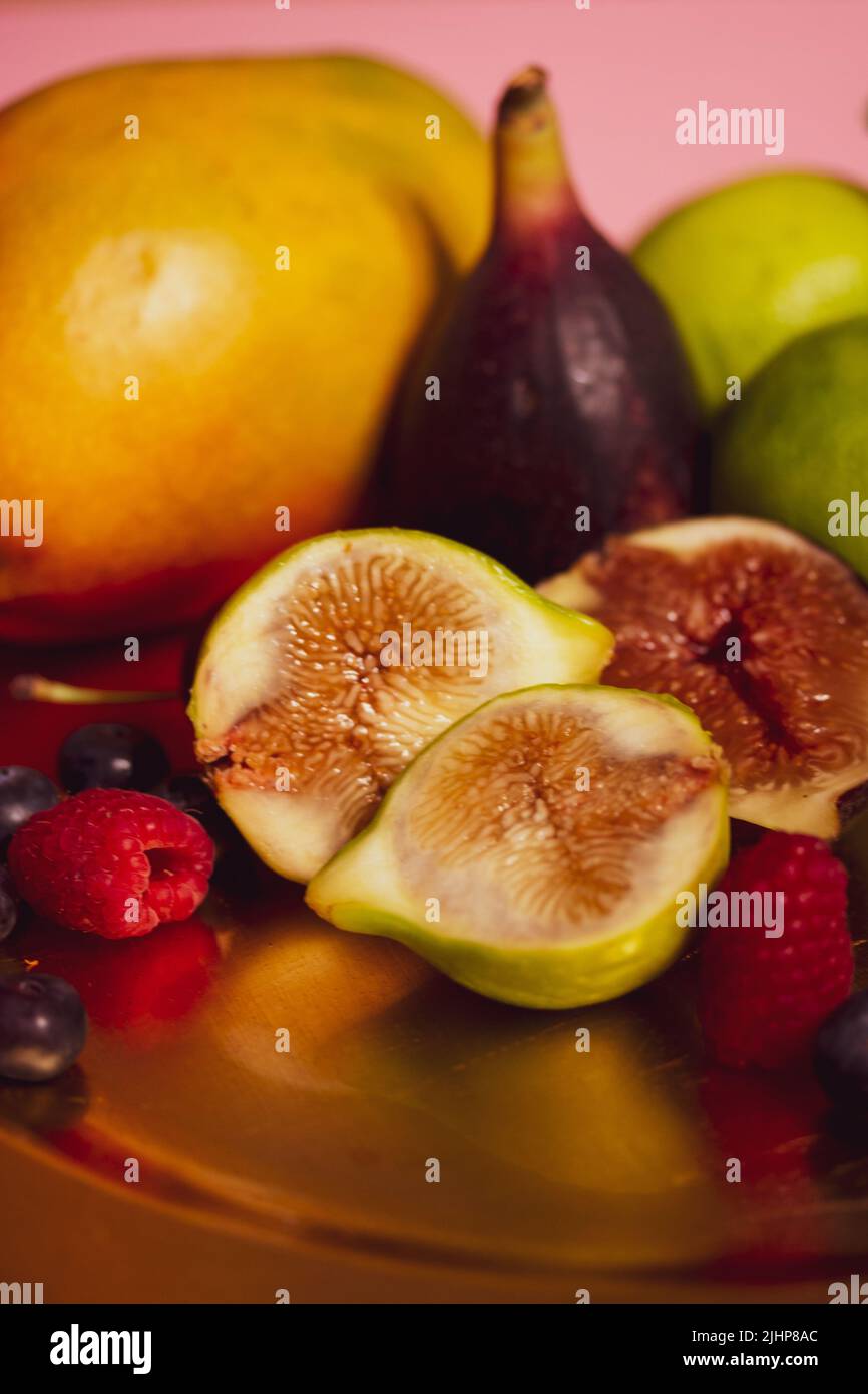 Un piatto d'oro, piatto di frutta tropicale fresca si trova su un tavolo. Fichi tagliati a metà, mango, lime e frutti di bosco di stagione, lamponi. Varietà di s. Foto Stock