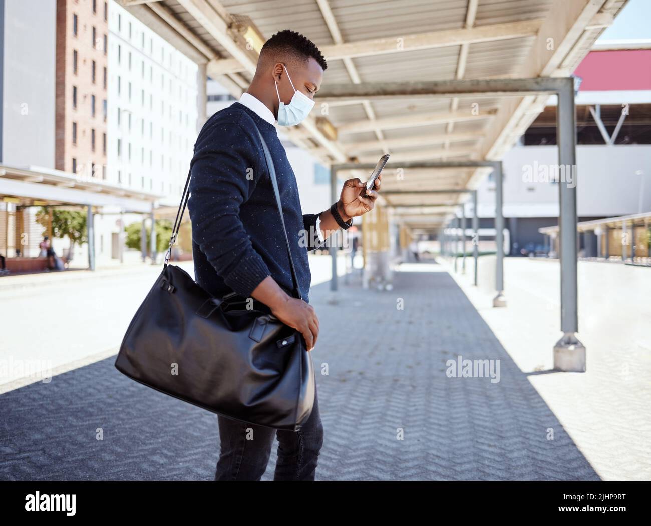 Uomo d'affari nero che viaggia da solo. Un giovane uomo d'affari afroamericano in attesa di un treno in una stazione ferroviaria e utilizzando il suo cellulare wireless Foto Stock