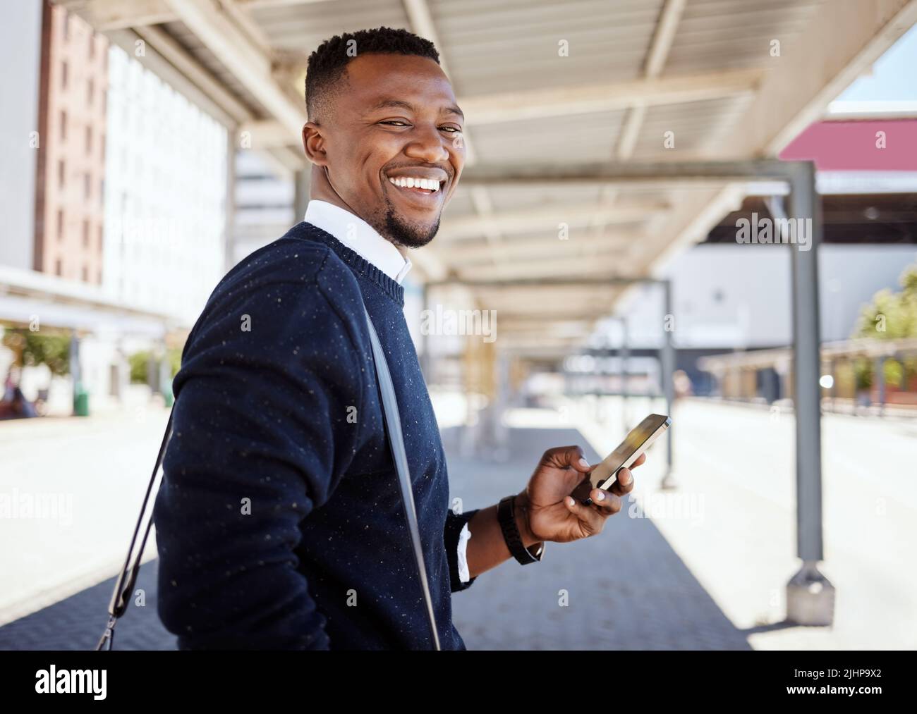 Ritratto di uomo d'affari nero che viaggia da solo. Un giovane uomo d'affari afroamericano in attesa di un treno in una stazione ferroviaria e utilizzando il suo wireless Foto Stock
