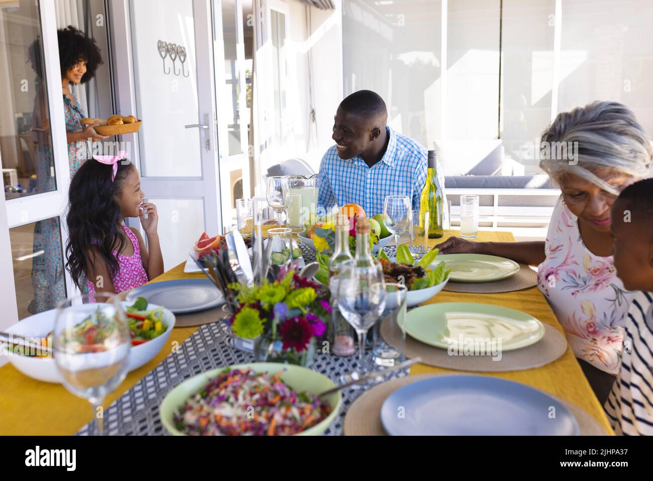 Famiglia multirazziale felice di parlare mentre si siede al tavolo da pranzo durante l'ora di pranzo Foto Stock