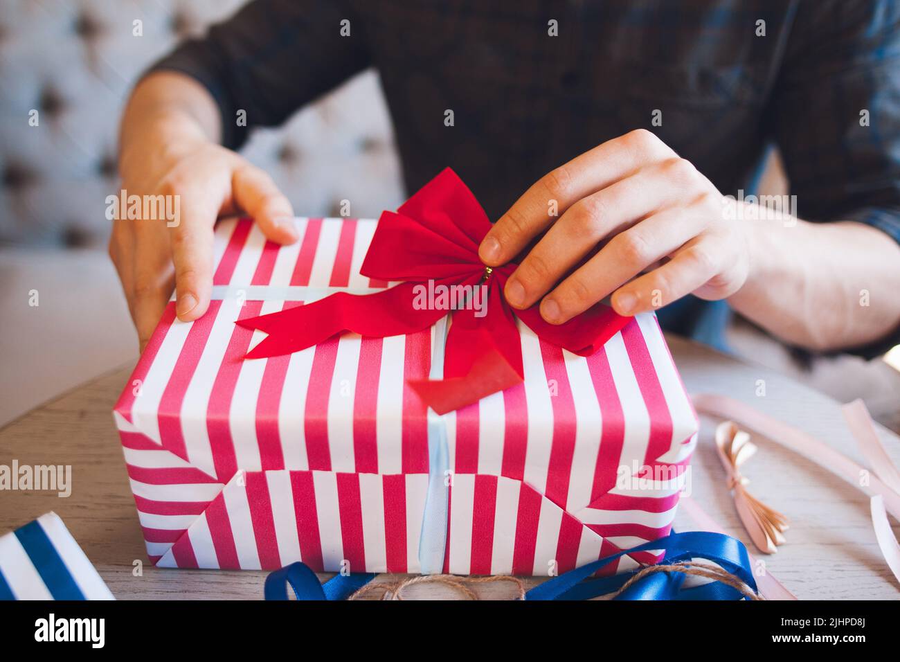 Uomo che decora scatola regalo con arco rosso Foto Stock