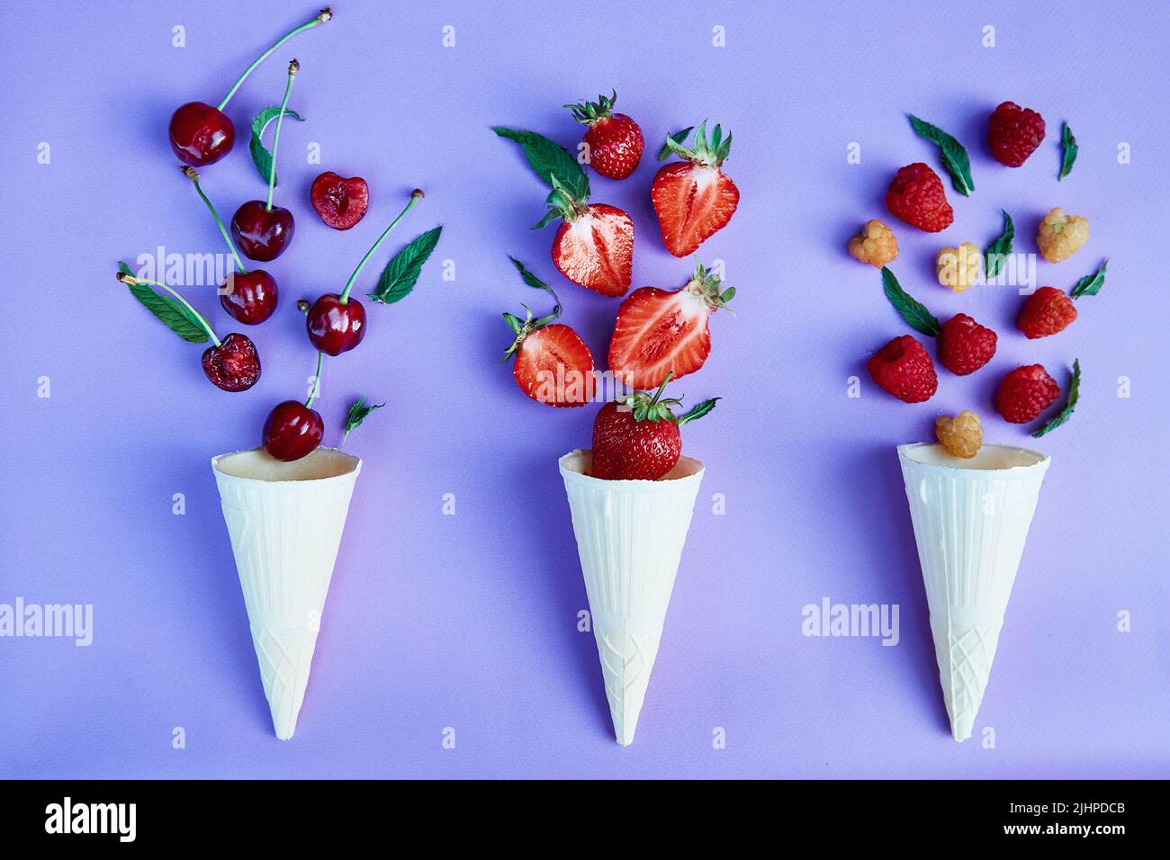 Spruzzi di fragole estive - fragole, lamponi e ciliegia da coni gelato su sfondo blu. Estate tempo cibo piatto laici. Foto Stock