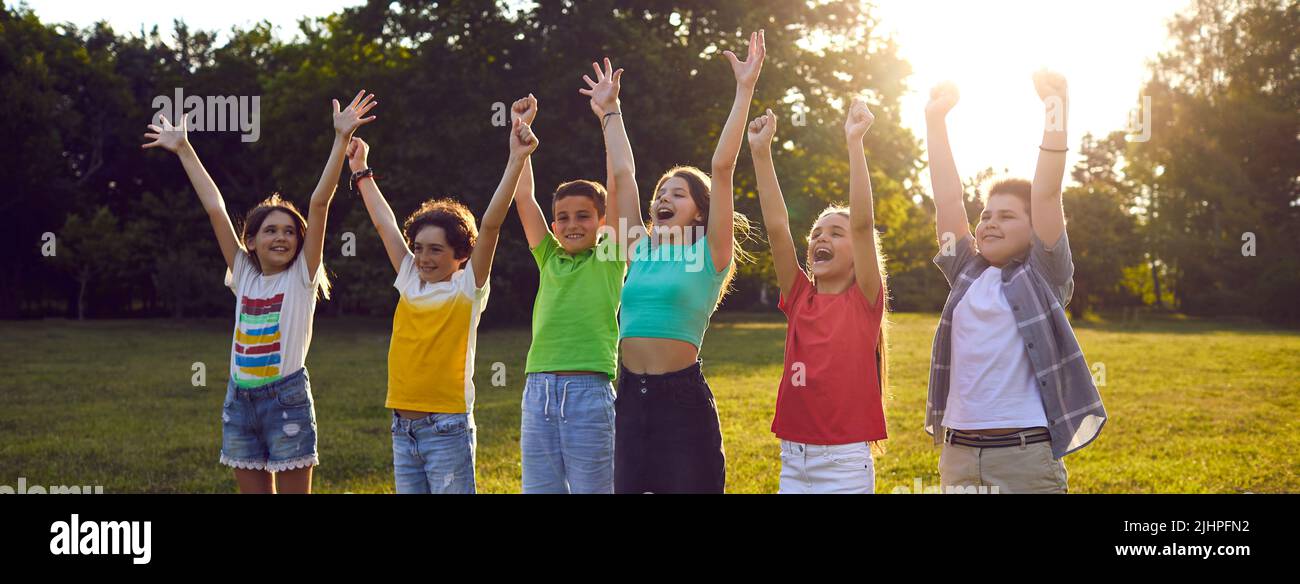 I bambini felici emozionalmente ed eccitati esclamano alzarsi le mani durante l'intrattenimento nel parco estivo Foto Stock