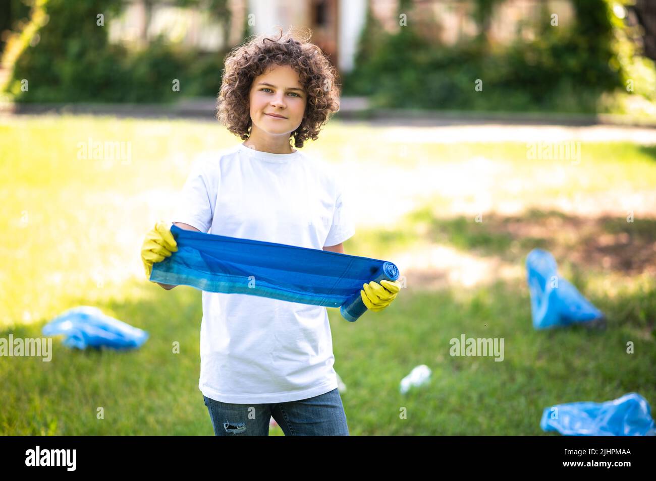 Teen in thsirt bianco in piedi sull'erba tra bottiglie di plastica Foto Stock