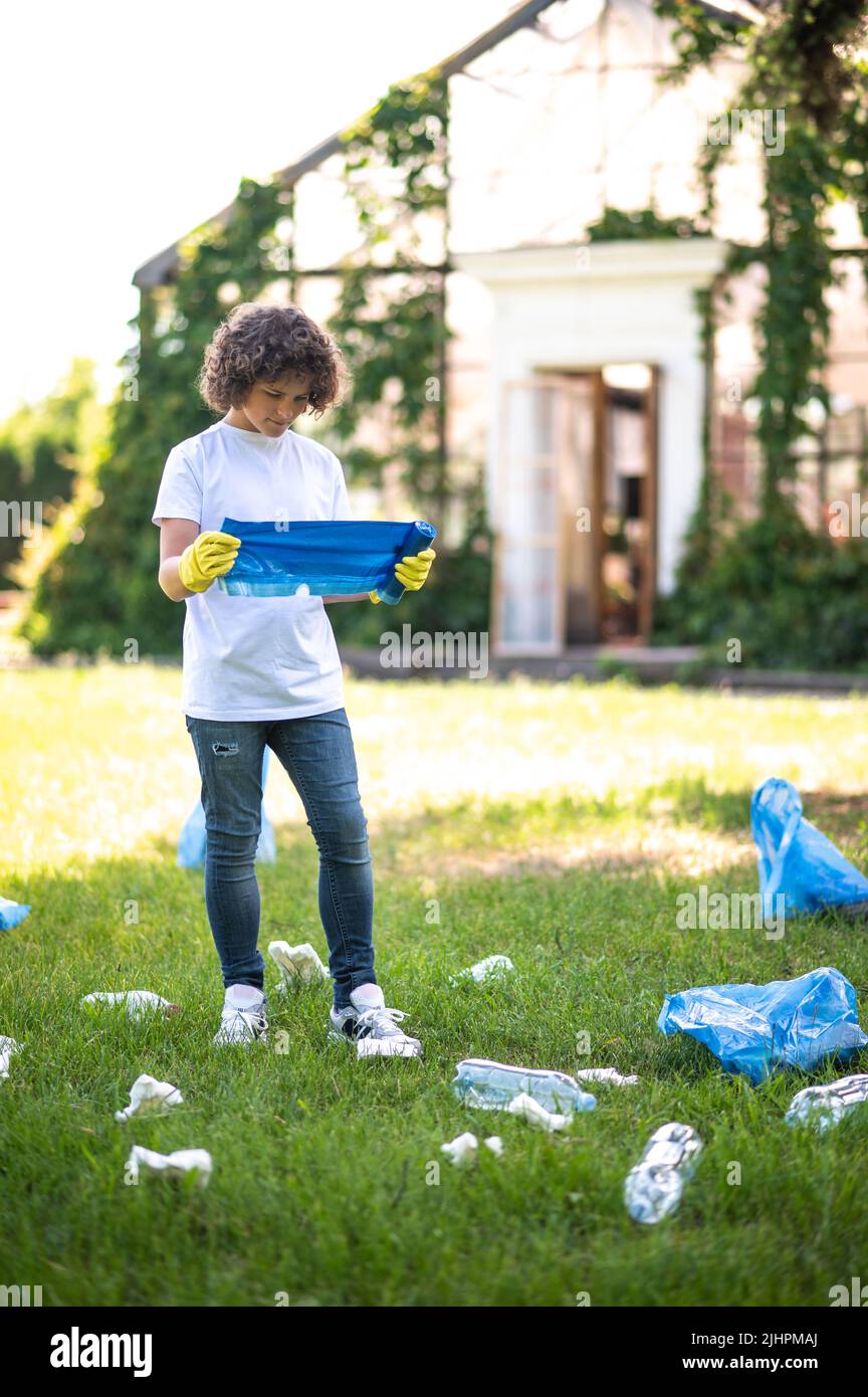 Teen in thsirt bianco in piedi sull'erba tra bottiglie di plastica Foto Stock