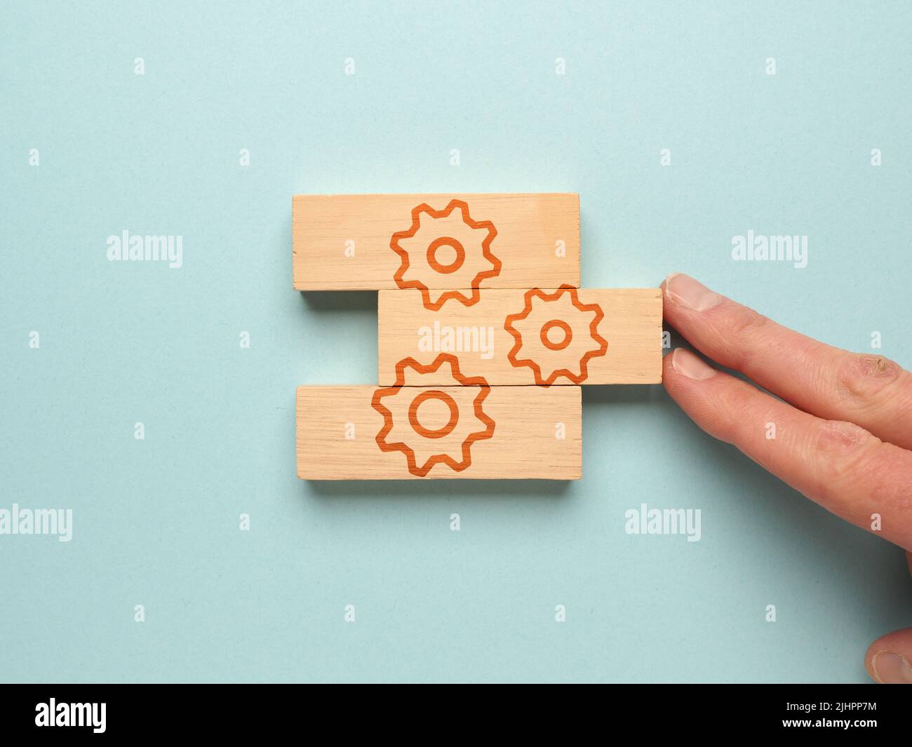 Blocchi di legno con un'icona a forma di ingranaggio su sfondo blu, una mano mette insieme i blocchi di legno Foto Stock