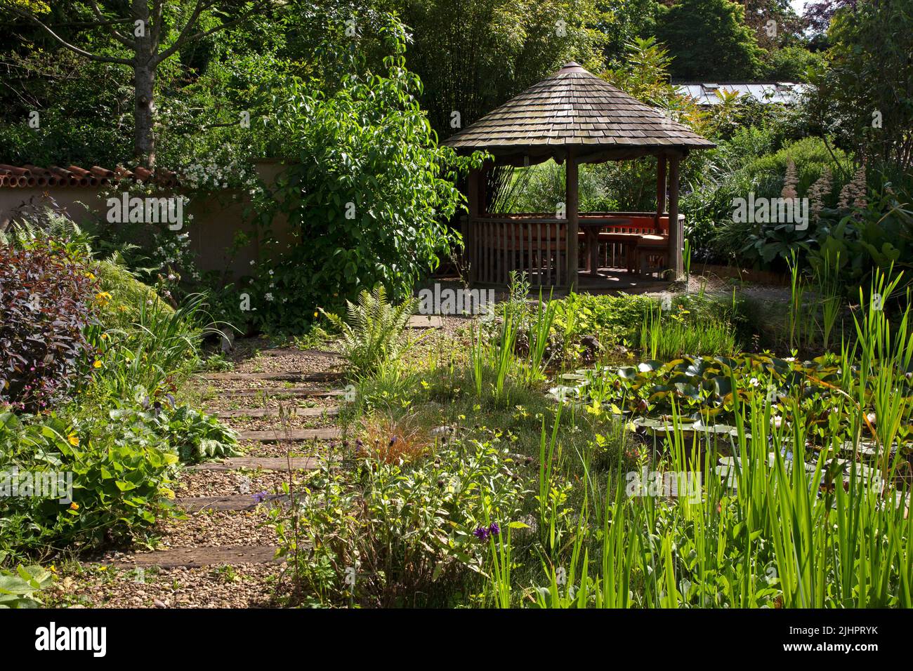 Giardino all'inglese con laghetto ornamentale con caratteristica Summerhouse e percorso in ghiaia con traversine in legno, Inghilterra Foto Stock