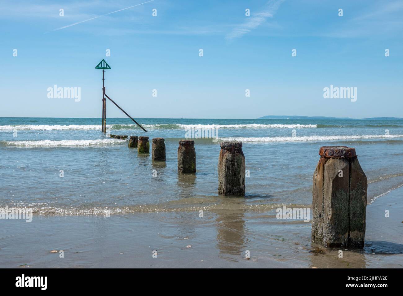 Vecchi groynes di legno che conducono giù ad una saracinesca di mare un contrassegno di navigazione su una spiaggia deserta bella a West Wittering Inghilterra con un'estate blu s. Foto Stock