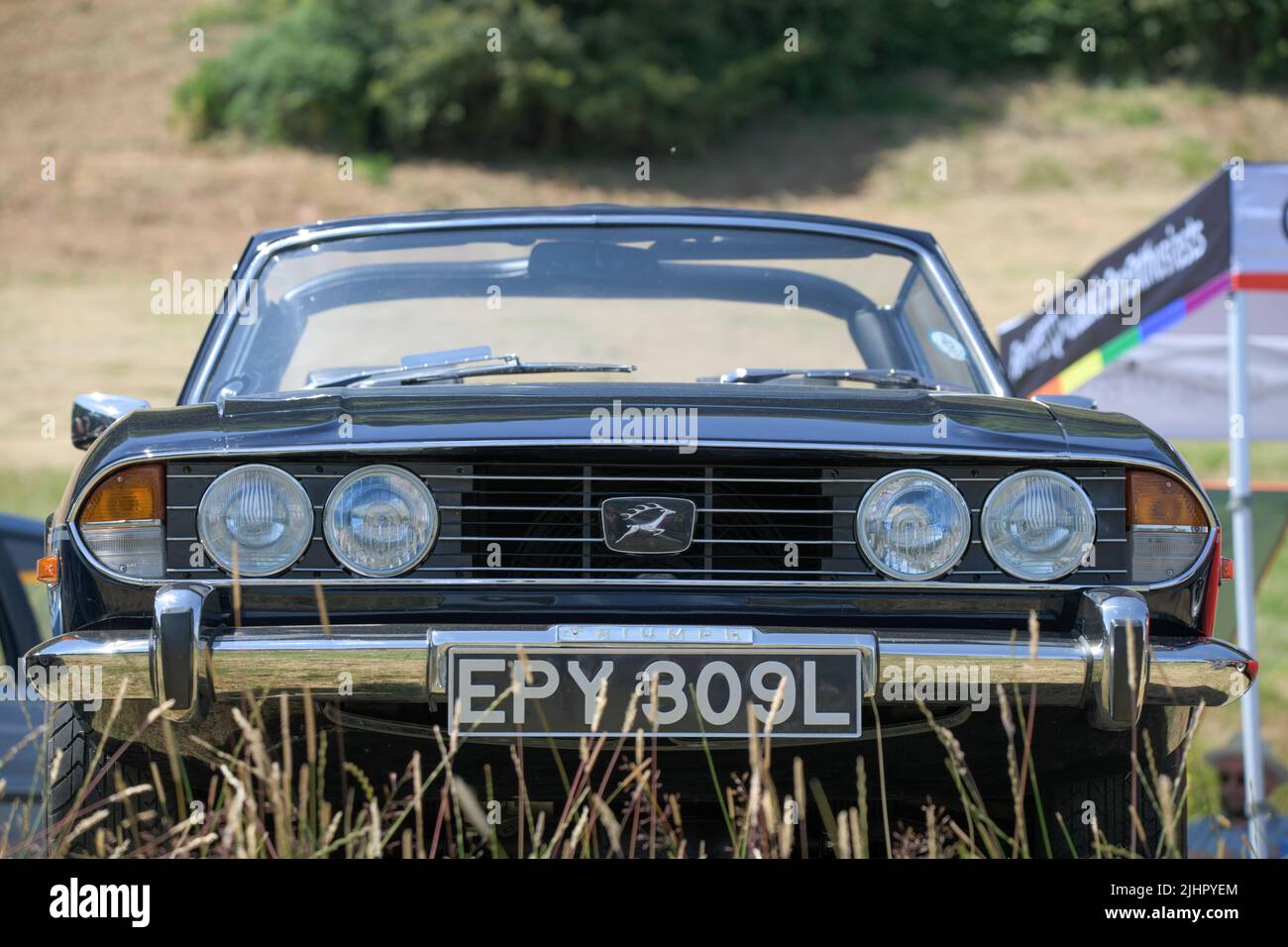 Vista frontale di una Triumph Stag nera e convertibile del 1970s nel mezzo di erba lunga Foto Stock