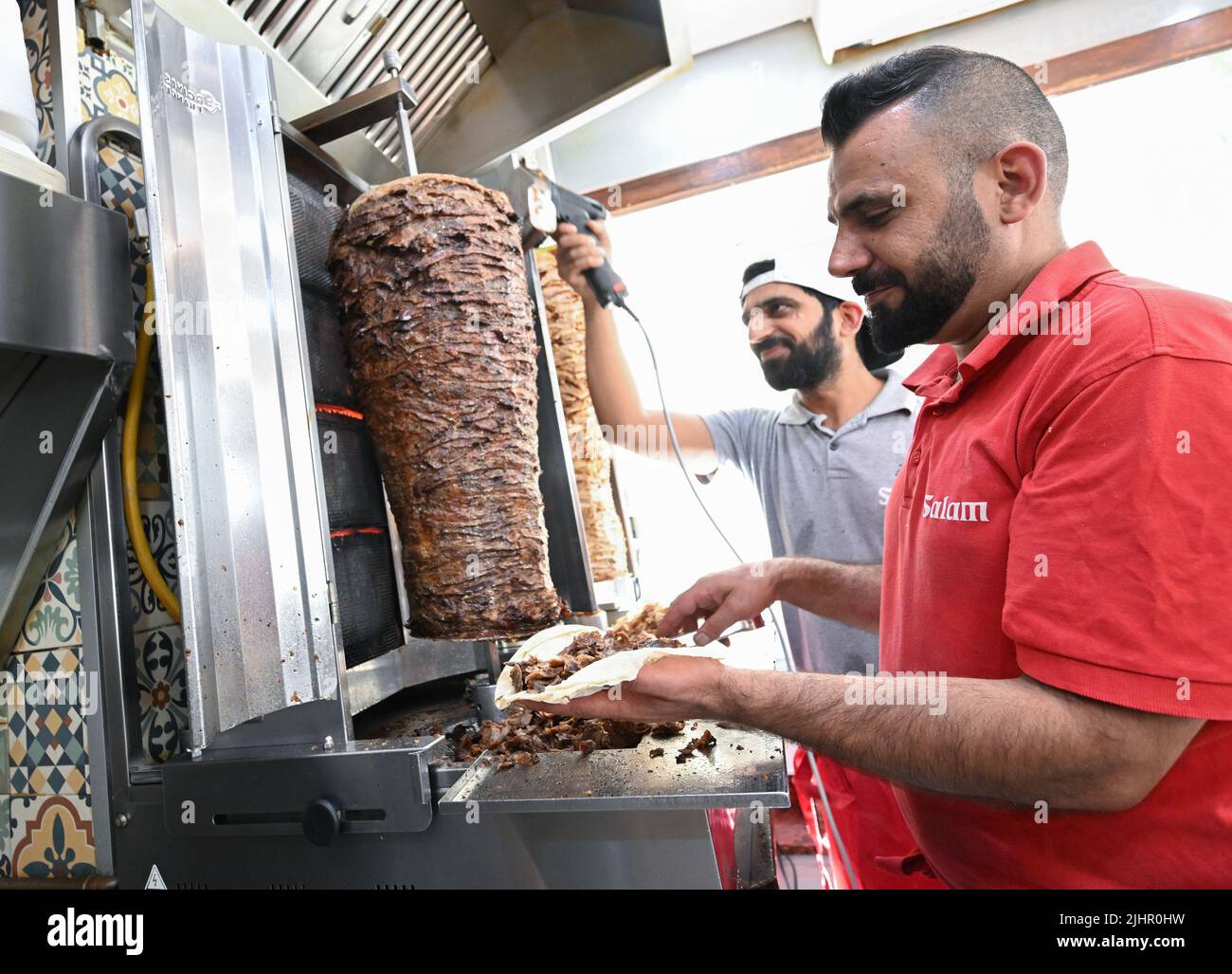 20 luglio 2022, Baden-Wuerttemberg, Tübingen: A metà estate le temperature esterne e circa 60 gradi Celsius alla griglia, due dipendenti di un ristorante kebab preparano kebab. Foto: Bernd Weißbrod/dpa Foto Stock