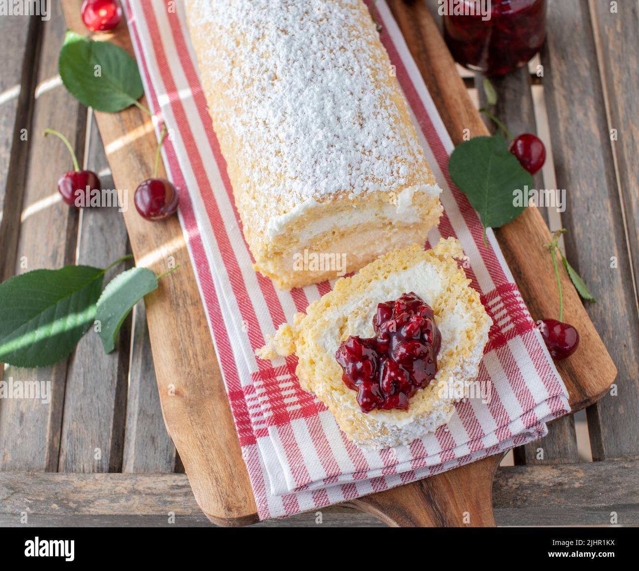 Dessert alla ciliegia con un rotolo svizzero ripieno di panna montata e condito con compote Foto Stock