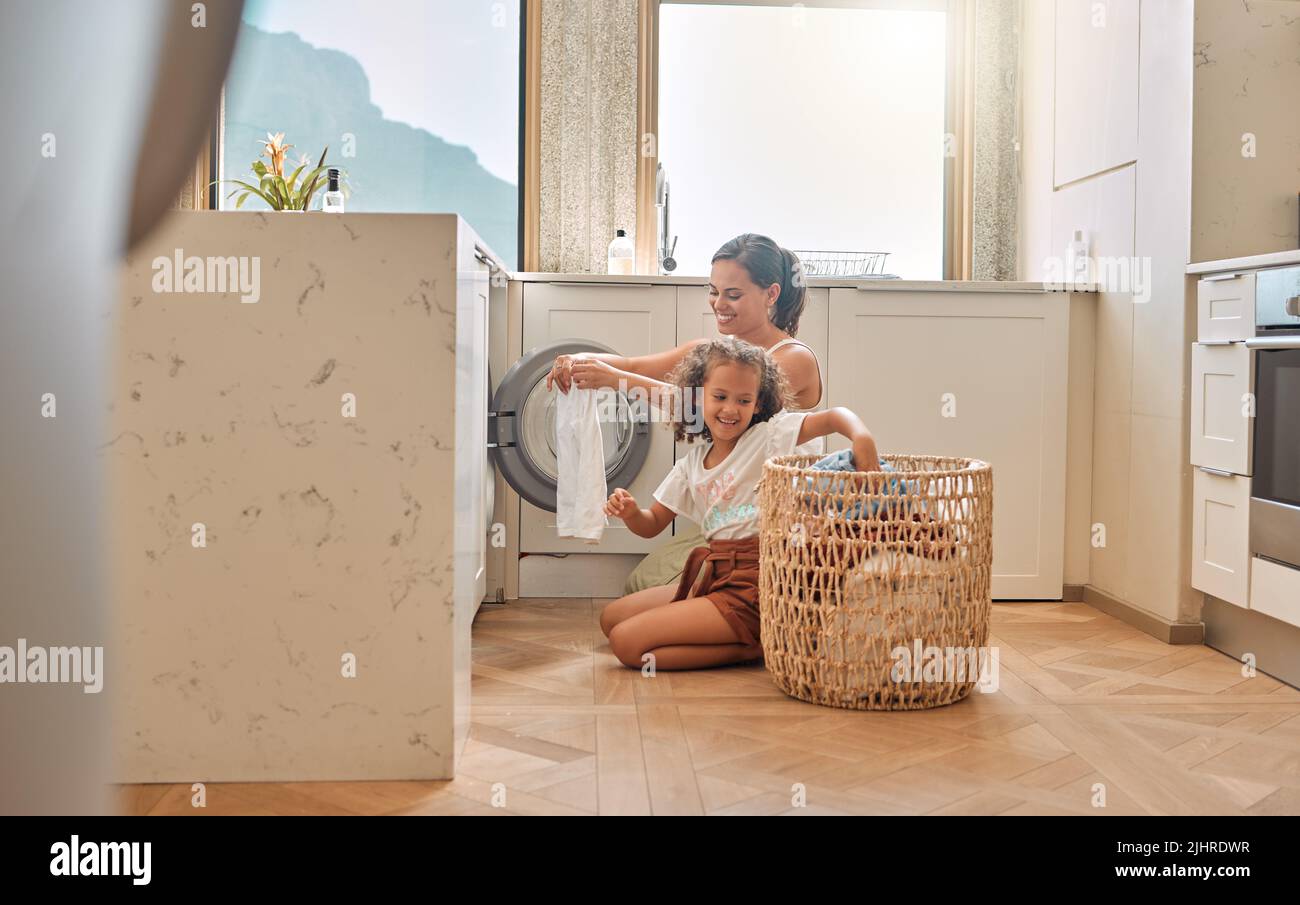 La giovane madre ispanica e sua figlia che smistano la biancheria sporca nella lavatrice a casa. Adorabile bambina e sua madre che fanno i compiti insieme Foto Stock