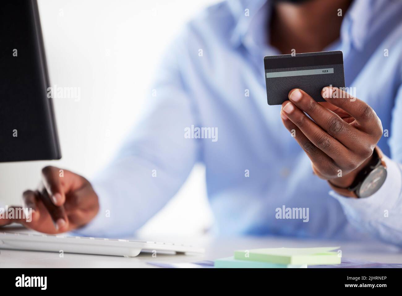 Primo piano di un uomo d'affari afroamericano che spende i soldi in linea con una carta di credito ed un calcolatore in un ufficio. Effettuare una transazione di acquisto con Foto Stock