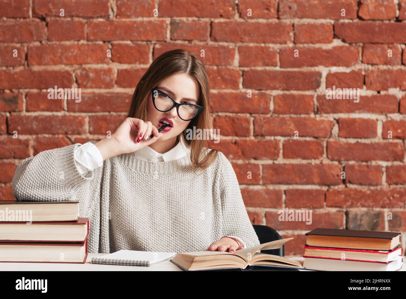 Bella ragazza studentesca che morde la penna alla biblioteca Foto Stock