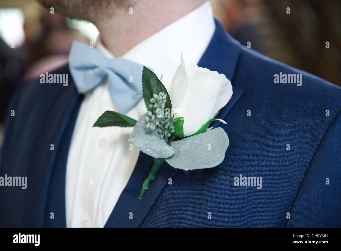 Un primo piano di uno sposo con un abito blu e un bowtie blu con un fiore spilla Foto Stock