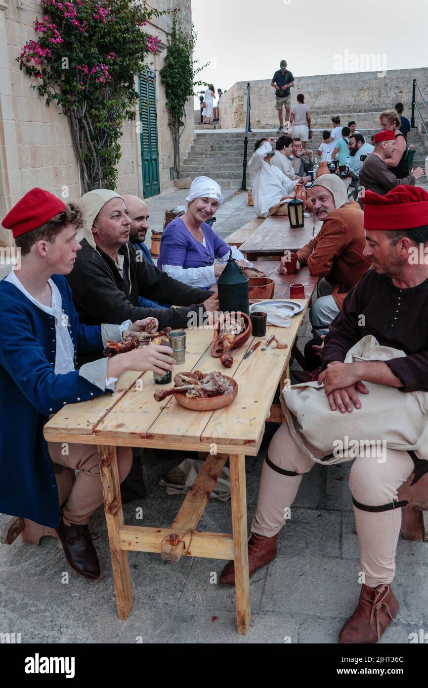 Persone che hanno un pasto con le posate appropriate in una rievocazione della vita medievale a Mdina, Malta, Mediterraneo Foto Stock
