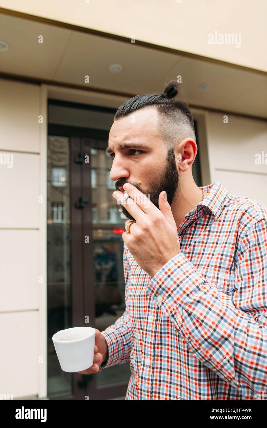 Giovane hipster fumando con una tazza di caffè all'aperto Foto Stock