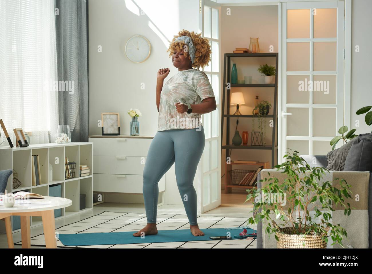 Ragazza africana in piedi su materassino di esercitazione e ballando alla musica durante l'addestramento di sport in casa Foto Stock