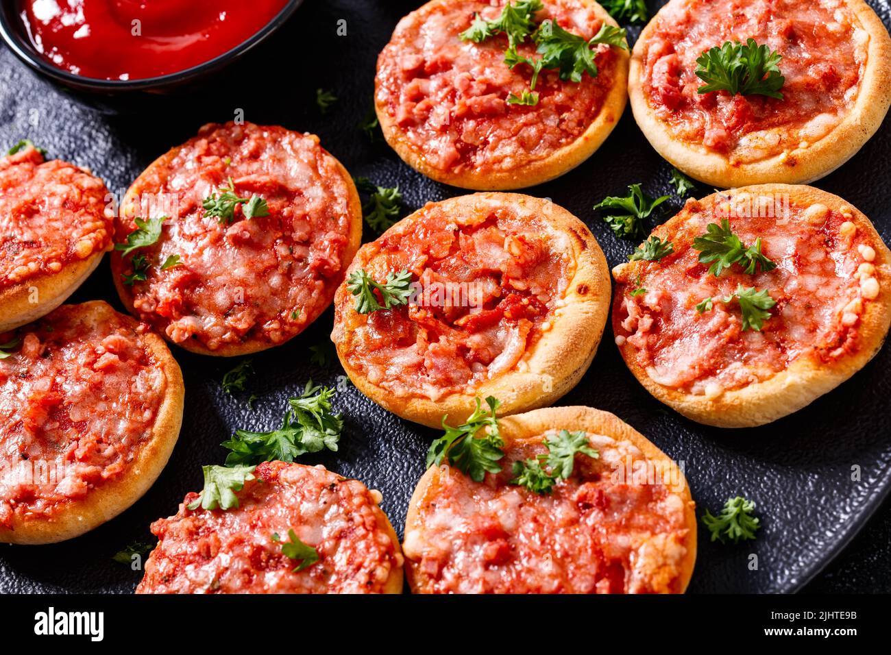 mini pizze, piccolinis, con prosciutto e pecorino su piatto nero con salsa di pomodoro, primo piano Foto Stock