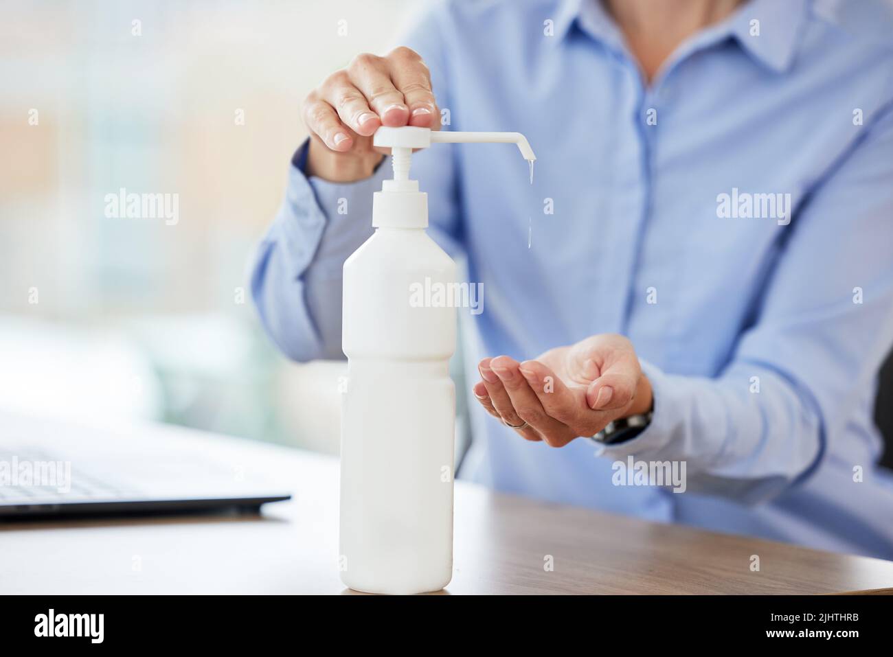 Primo piano delle mani femminili utilizzando l'igienizzatore sul posto di lavoro. Bottiglia di gel di alcool posta sulla scrivania in ufficio per pulire le mani e uccidere o prevenire la diffusione di Foto Stock
