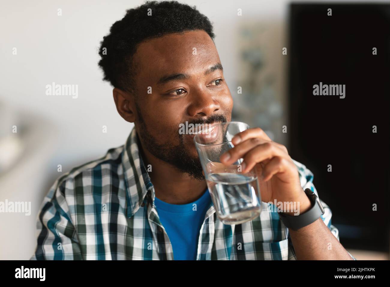 Happy Millennial African American Man bere acqua seduta a casa Foto Stock