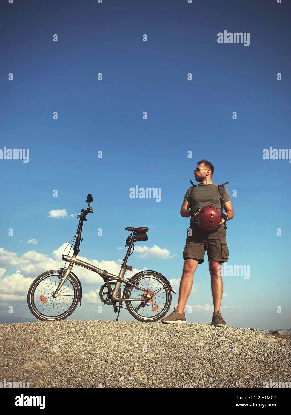 Uomo con magliette pieghevoli per biciclette, occhiali da sole e casco su sfondo cielo blu. Foto Stock