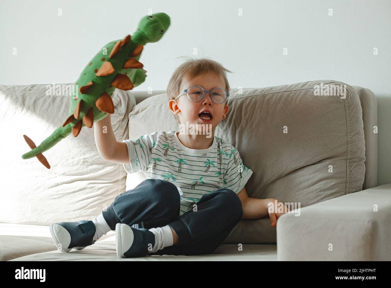 Un bambino con autismo in occhiali siede sul divano e triste, arrabbiato a. Foto Stock