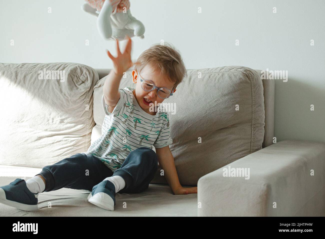 Un bambino con autismo in occhiali siede sul divano e triste, arrabbiato a. Foto Stock