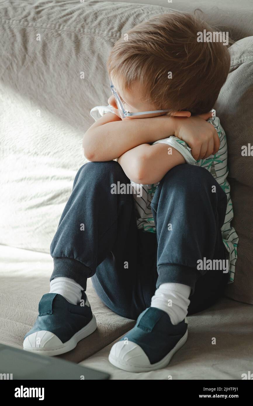Bambino con autismo in occhiali siede sul divano e triste Foto Stock