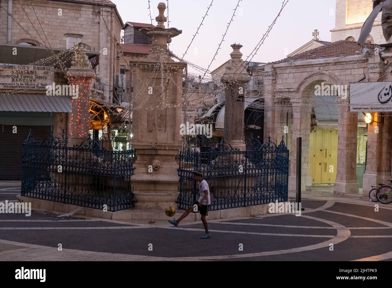 Un giovane colono ebreo gioca con un calcio accanto alla fontana costruita in stile neo barocco nel 1903 per celebrare il 25th anniversario del dominio del Sultano Abdul Hamid al mercato Aftimos nell'area del Muristan nel quartiere cristiano, nella città vecchia di Gerusalemme est Israele Foto Stock