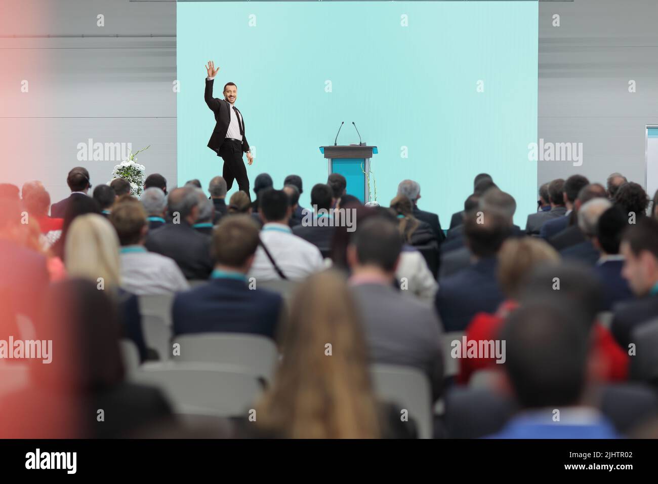 Un uomo d'affari che sventolano sul palco e la gente che guarda al pubblico durante una conferenza Foto Stock